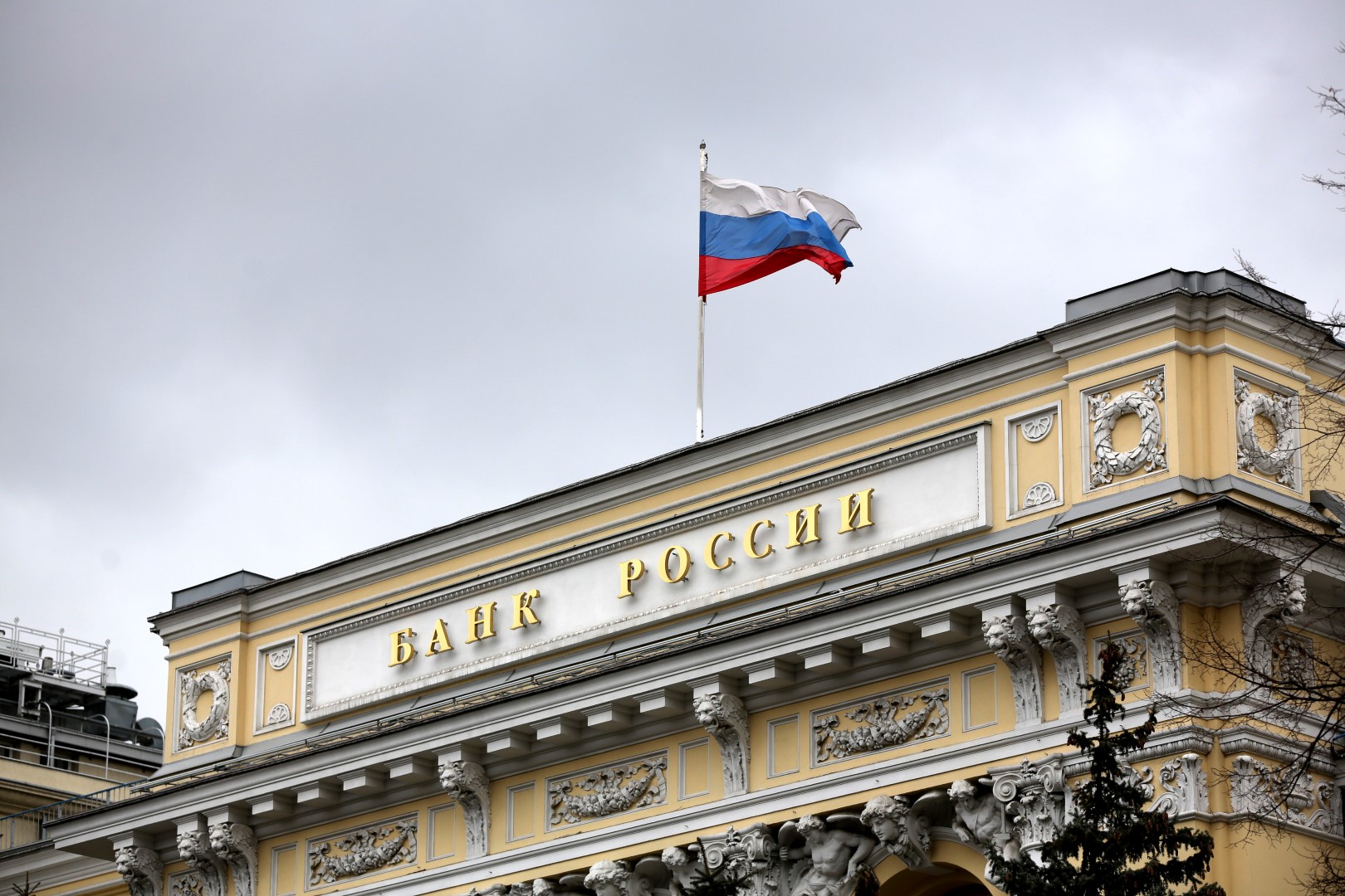 The flag of the Russian Federation flies above the headquarters of the Russian central bank, also known as Bank Rossii, in Moscow, Russia, on Friday, March 18, 2016. Russia's central bank kept its benchmark interest rate unchanged for a fifth meeting amid risks to inflation, warning that its "moderately tight" monetary policy may last longer than previously planned. Photographer: Andrey Rudakov/Bloomberg