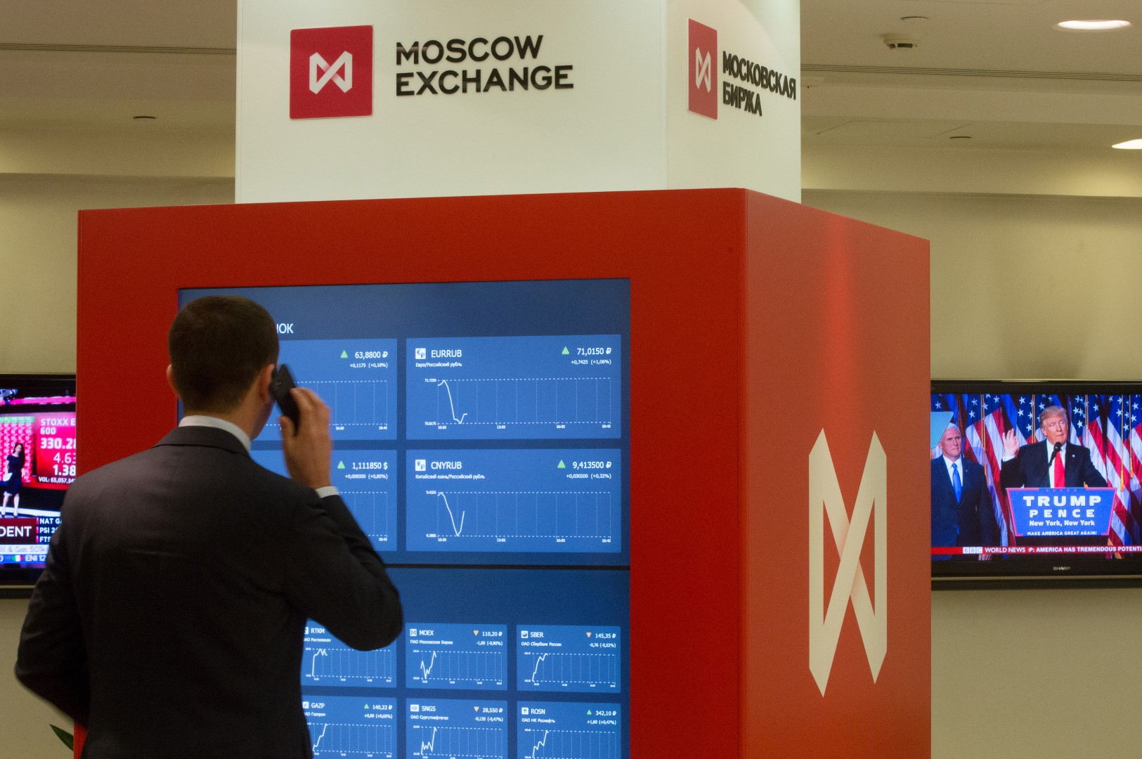 A visitor speaks on a smartphone while looking at financial information screens showing market reaction to the U.S. presidential election results at the Moscow Exchange in Moscow, Russia, Nov. 9, 2016. The ruble dropped as Donald Trump won the U.S. presidential race, driving down crude prices on concern his protectionist policies will sap global growth. Photographer: Andrey Rudakov/Bloomberg