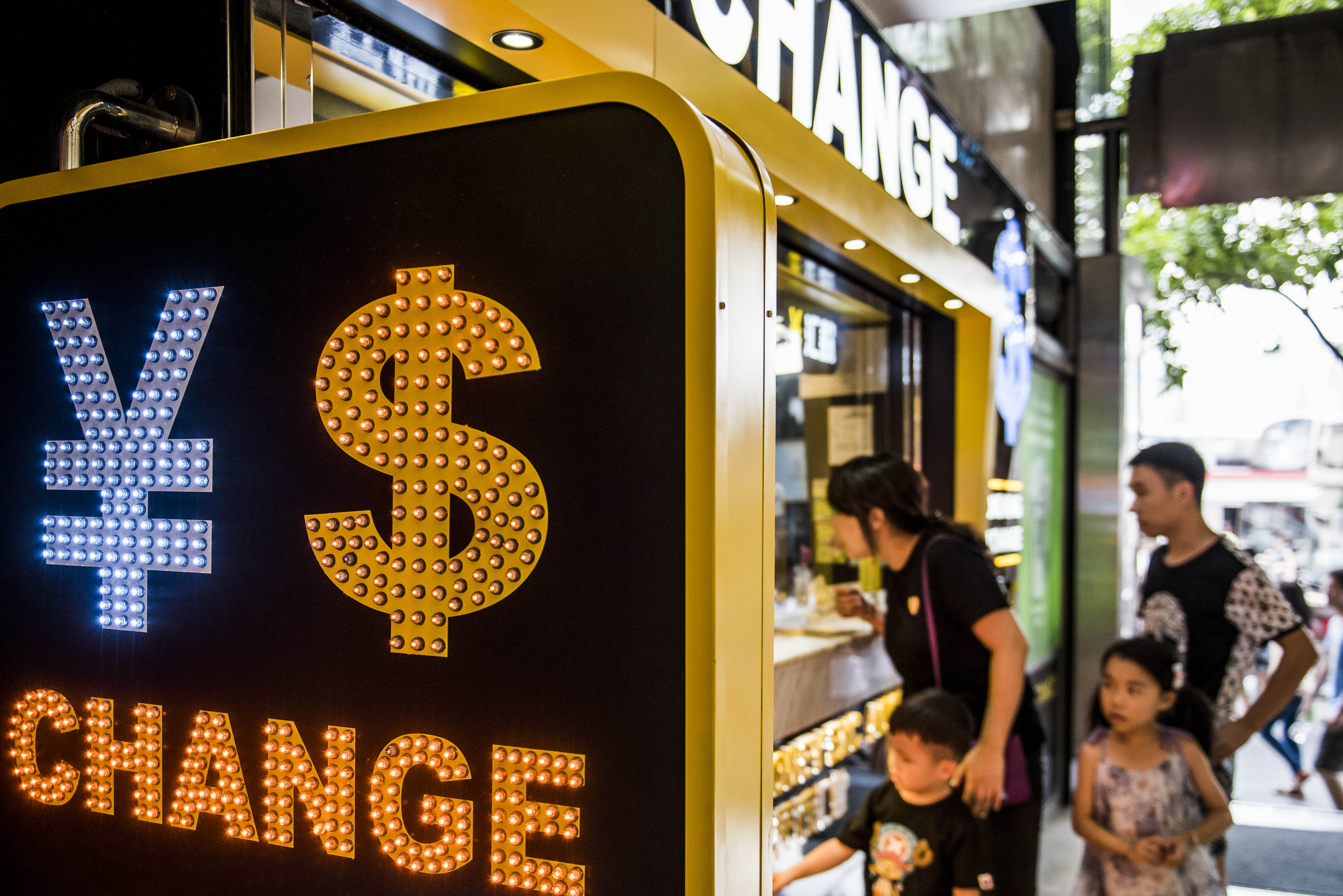 The currency symbol for the Chinese yuan and the dollar is displayed at a currency exchange store in Hong Kong, China, on Wednesday, Aug. 12, 2015. The yuan sank for a second day, spurring China's central bank to intervene as the biggest rout since 1994 tested the government's resolve to give market forces more sway in determining the exchange rate. Photographer: Xaume Olleros/Bloomberg