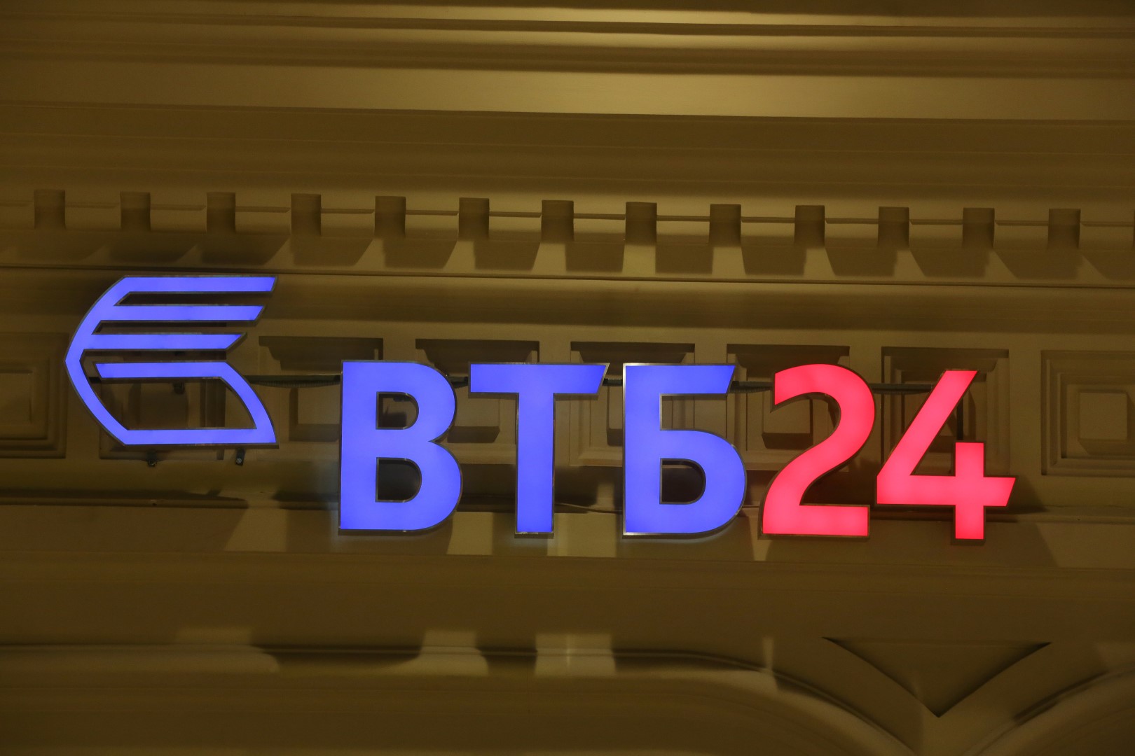 An illuminated sign for Bank VTB 24, a retail unit of state-controlled VTB Group, sits on display above an automated teller machine (ATM) outlet in Moscow, Russia, on Monday, Dec. 22, 2014. The ruble's rout, sparked by falling oil prices and sanctions imposed on businesses including OAO Sberbank, prompted Russians to begin buying luxury goods from Porsche sports cars to Tiffany rings to preserve the value of their savings. Photographer: Andrey Rudakov/Bloomberg