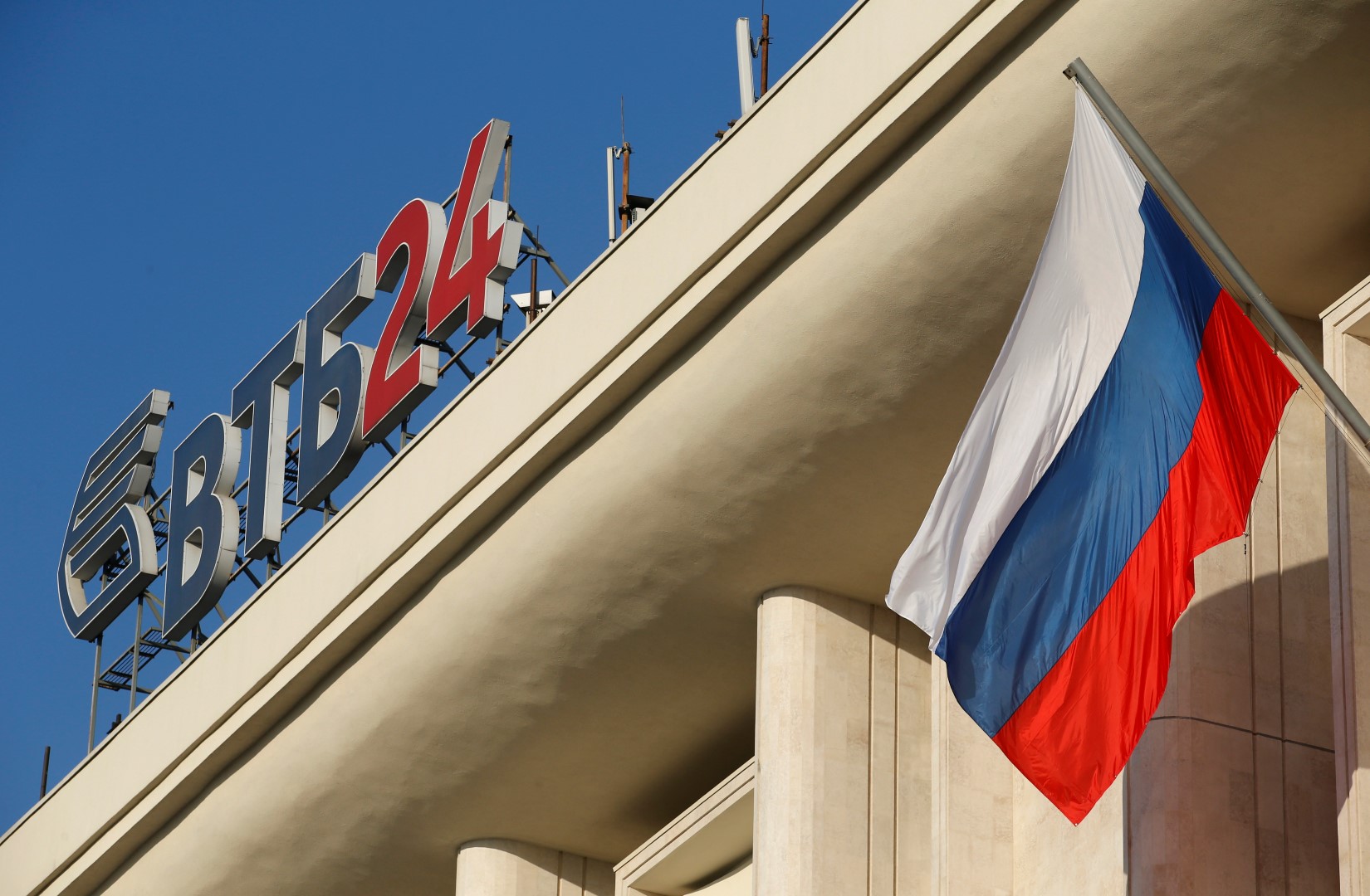 The logo of VTB Bank is displayed on the roof of a building, with a Russian national flag seen nearby, in Moscow, November 20, 2014. Russia's second-largest bank VTB said on Thursday its third-quarter net profit fell 98 percent year-on-year, dragged lower by higher provisions for bad loans and an economic slowdown. REUTERS/Maxim Zmeyev (RUSSIA - Tags: BUSINESS LOGO) - RTR4EUSH